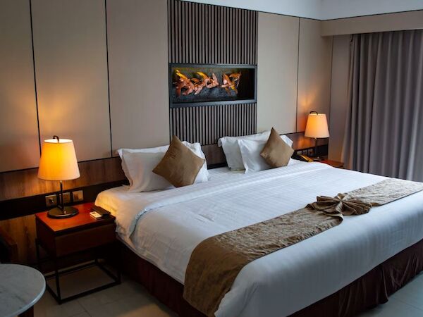This image shows a neatly made hotel room bed with two nightstands, lamps, decorative pillows, and a wall art piece above the headboard.