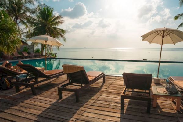 A serene poolside scene with lounge chairs, umbrellas, and a stunning view of the ocean under a partly cloudy sky, creating a tranquil atmosphere.