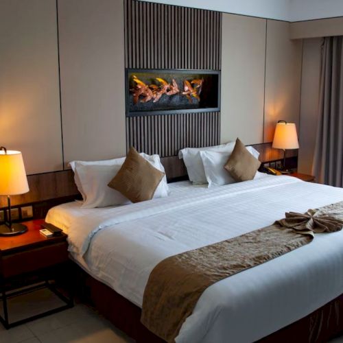 A neatly arranged hotel room with a large bed, side tables with lamps, a wall-mounted decor piece, and a window with curtains drawn to the side.