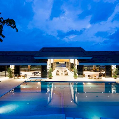A luxurious outdoor swimming pool area at dusk, set in front of a modern building with open spaces and ambient lighting.