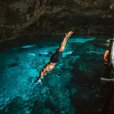 A person is diving into clear, blue water inside a cave or cenote, exhibiting a picturesque and adventurous underwater scene.