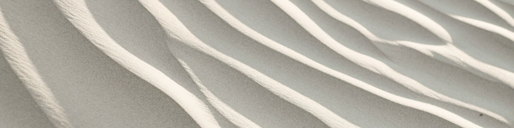 The image shows sand dunes with wavy patterns formed by the wind, creating a textured and abstract landscape.