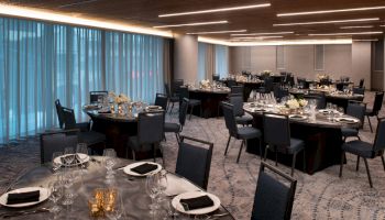 The image shows a dimly-lit banquet hall with multiple round tables set for a formal event, featuring black tablecloths, place settings, and floral centerpieces.