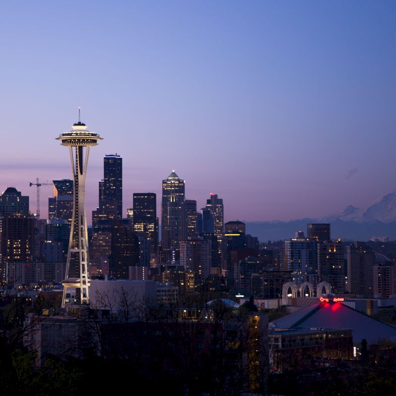 This image shows the skyline of Seattle at dusk with the Space Needle prominently featured and Mount Rainier in the background.