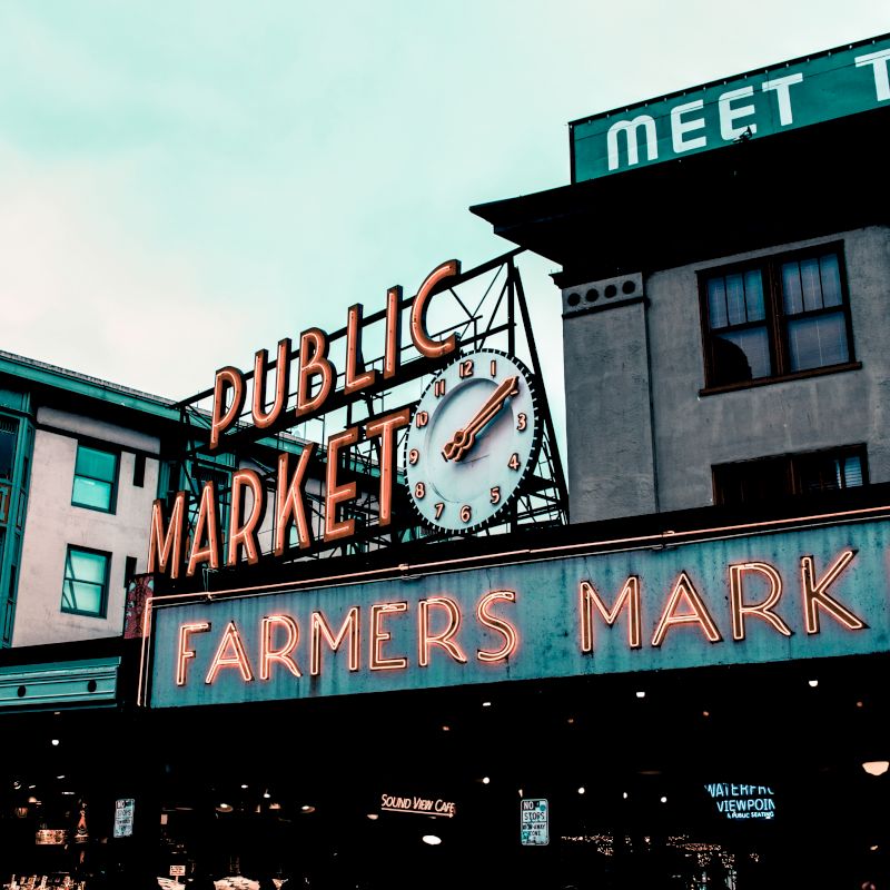 The image shows a famous public market with neon signs reading "Public Market" and "Farmers Market" on buildings, creating a nostalgic ambiance.