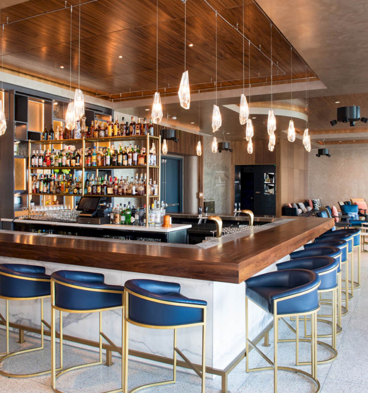 A modern bar with stylish seating, a well-stocked assortment of spirits, and ambient lighting fixtures. Comfortable seating areas in the background.