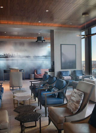 A modern lounge with comfortable seating, large windows offering a scenic view of a ferris wheel and water, and stylish minimalist decor.