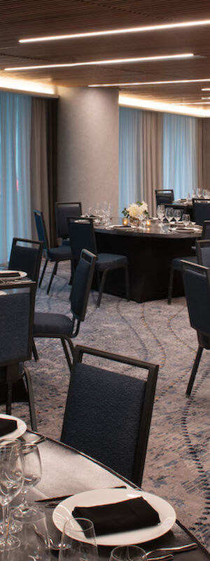 A beautifully set banquet hall with round tables, elegant place settings, and floral centerpieces. Dim lighting and modern decor create a sophisticated ambiance.