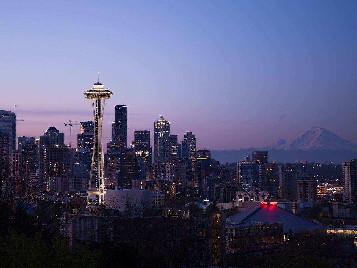 This image shows the Seattle skyline at twilight, featuring the Space Needle prominently, with Mount Rainier visible in the background.