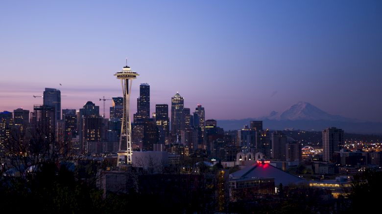 This image shows the Seattle skyline at twilight, featuring the Space Needle prominently, with Mount Rainier visible in the background.